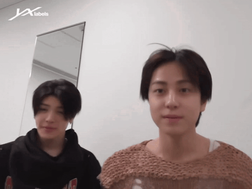 Two Men Standing In Front Of JX Labels Wall GIF