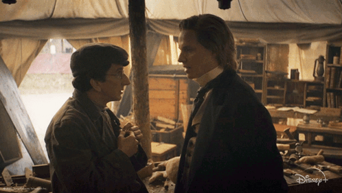 Two Men Standing Next To Each Other In A Room With A Disney+ Logo On The Bottom GIF
