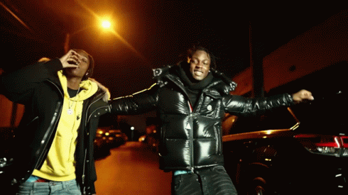 Two Men Standing Next To Each Other On A Street At Night GIF