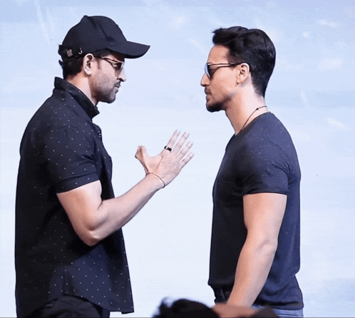 Two Men Standing Next To Each Other With One Wearing A Black Hat GIF