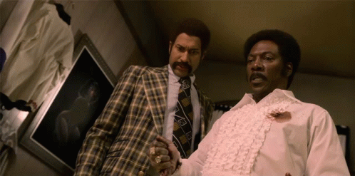 Two Men Standing Next To Each Other With One Wearing A White Shirt With Ruffles On The Sleeves GIF
