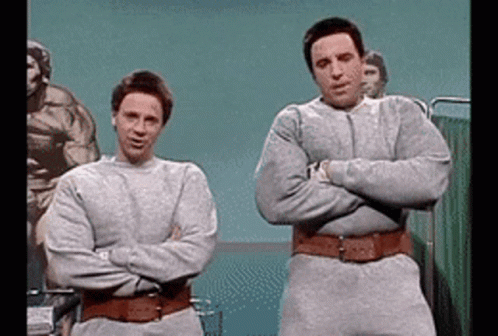 Two Men Standing Next To Each Other With Their Arms Crossed In A Hospital Room GIF