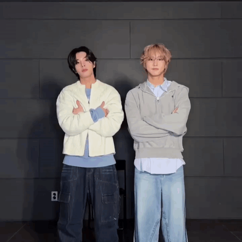 Two Men Standing Next To Each Other With Their Arms Crossed In Front Of A Wall With The Letter B On It GIF