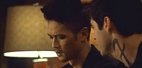 Two Men Standing, One With Neck Tattoo Saying X