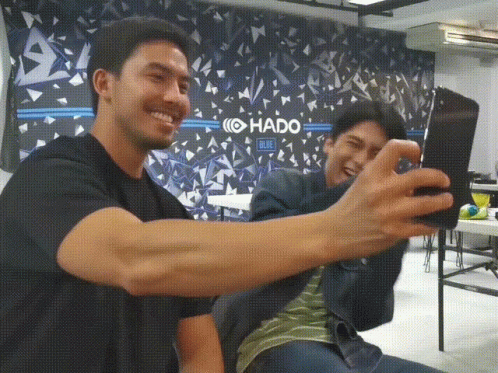 two men take a selfie in front of a wall that says hado blue