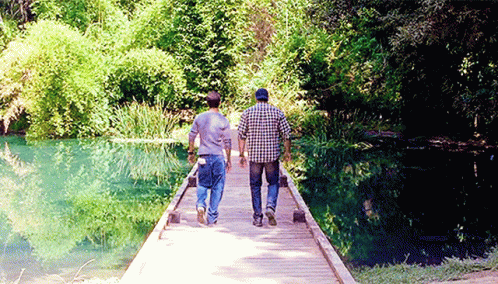 Two Men Walking Across Wooden Bridge Over River