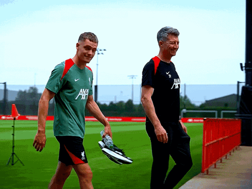 Two Men Walking on Field, One Wearing AXA Shirt