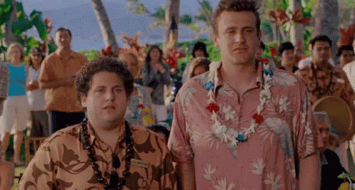 Two Men Wearing Hawaiian Shirts And Lei Are Standing Next To Each Other In Front Of A Crowd Of People . GIF