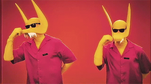 Two Men Wearing Pink Shirts And Yellow Masks With Horns Are Standing Next To Each Other On A Red Background GIF