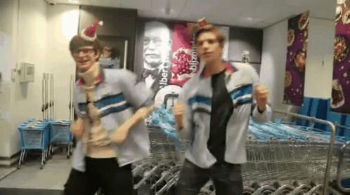 Two Men Wearing Santa Hats Dancing in Front of Sign Albert Blitzman