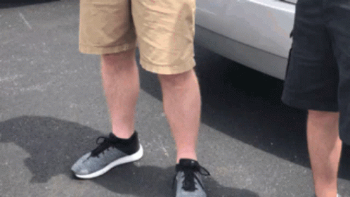 Two Men Wearing Shorts And Sneakers Are Standing Next To Each Other In Front Of A Car GIF