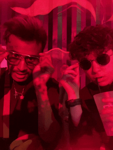 Two Men Wearing Sunglasses And Suspenders Pose For A Picture In A Dark Room GIF