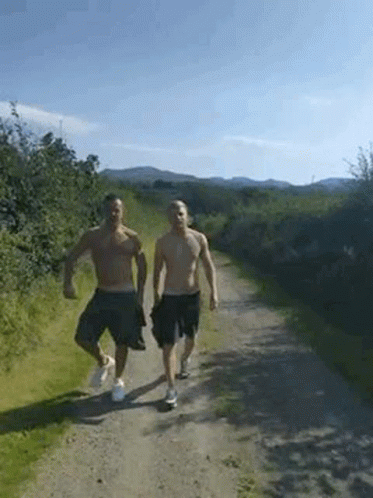 Two Men Without Shirts Are Walking Down A Dirt Road . GIF