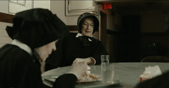 two nuns sit at a table eating food and drinking water