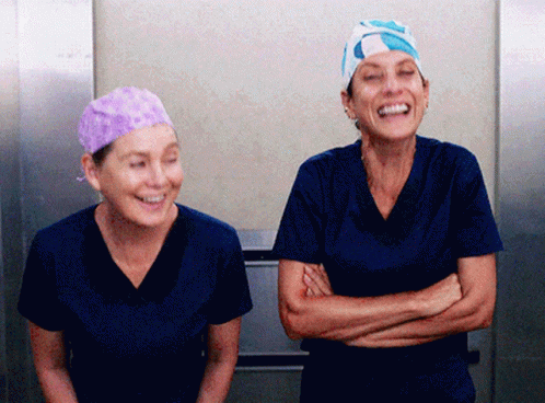 Two Nurses Wearing Scrubs And Hats Are Laughing Together GIF