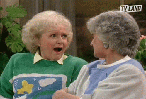 two older women are sitting next to each other and one is wearing a green sweater and the other is wearing a blue shirt