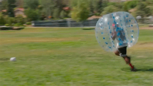 Two People Are Playing Bubble Soccer In A Field GIF