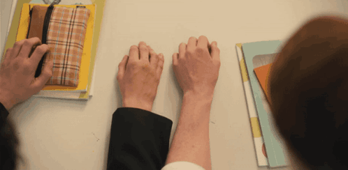 Two People Holding Hands On A Table With Books GIF