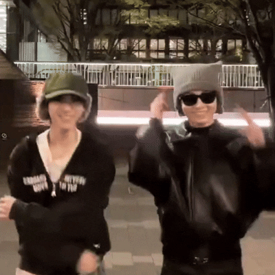 Two People In Hats And Sunglasses Dancing In Front Of Building With Fence GIF