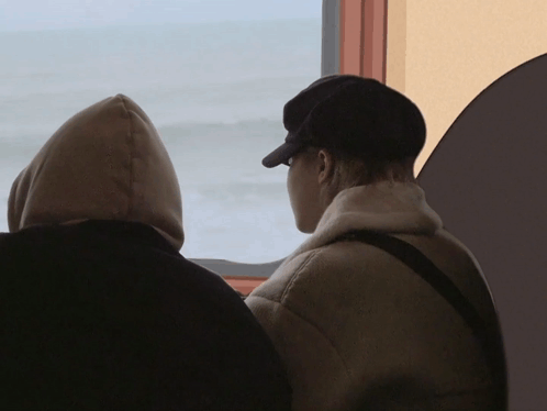 Two People Looking Out A Window With One Wearing A Hoodie GIF