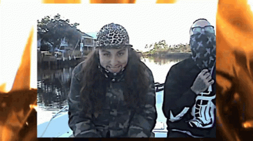 Two People On A Boat With One Wearing A Leopard Print Hat And The Other Wearing A Black Shirt With The Letter T On It GIF
