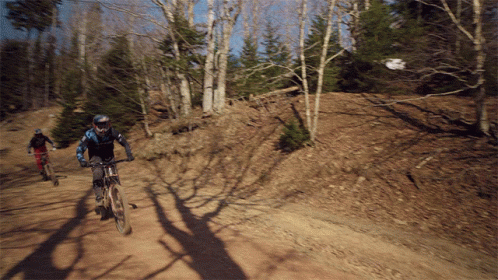 Two People Riding Bikes Down A Dirt Road GIF
