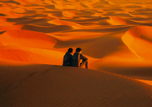 Two People Sitting on Sand Dune in Desert
