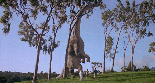 Two People Standing Before Giant Dinosaur GIF