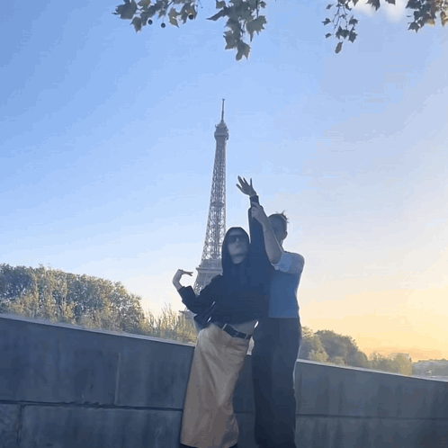 Two People Standing In Front Of The Eiffel Tower With Their Arms In The Air GIF