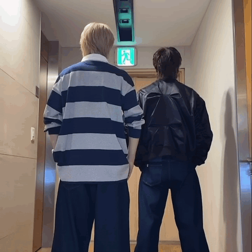 Two People Standing In Hallway With Exit Sign GIF