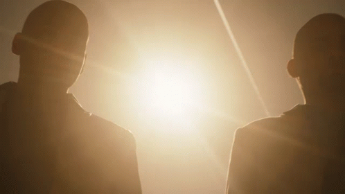 Two People Standing Next To Each Other In Front Of A Bright Light GIF