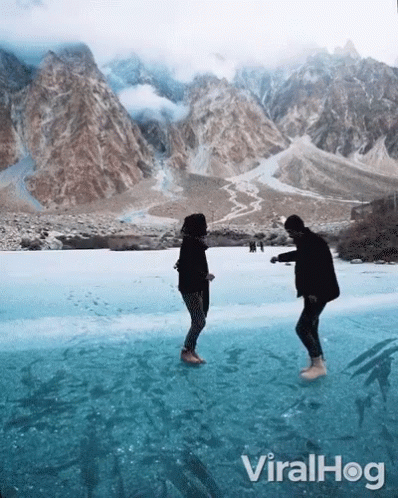 Two People Standing On A Frozen Lake With Mountains In The Background And The Words Viralhog On The Bottom Right GIF