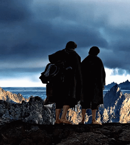 Two People Standing On Top Of A Rocky Cliff Looking Out Over A Body Of Water GIF