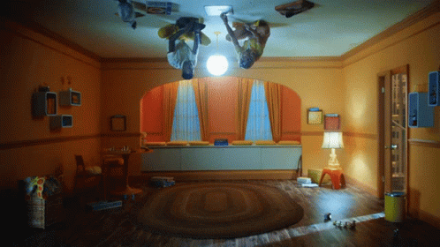 Two People Upside Down in Room With Lamp and Box Saying A