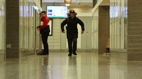Two People Walking Down A Hallway With A Sign That Says Jojo GIF
