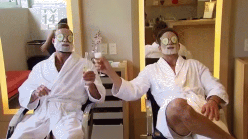 Two People Wearing Facial Masks Are Toasting With Champagne GIF