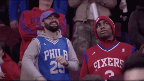 Two Philadelphia Sixers Fans Are Sitting In The Stands At A Basketball Game . GIF