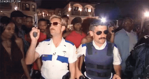Two Police Officers Are Standing In Front Of A Crowd Holding Guns .. GIF