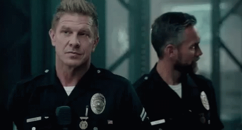 Two Police Officers Are Standing Next To Each Other In A Dark Room Looking At The Camera . GIF
