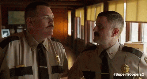 Two Police Officers Are Standing Next To Each Other In A Hallway Talking To Each Other . GIF