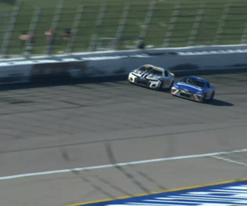 Two Race Cars Racing On Track With White Fence GIF