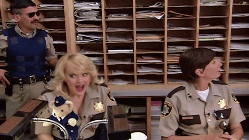 Two Sheriff 'S Officers Are Sitting At A Desk With A Teddy Bear On It GIF