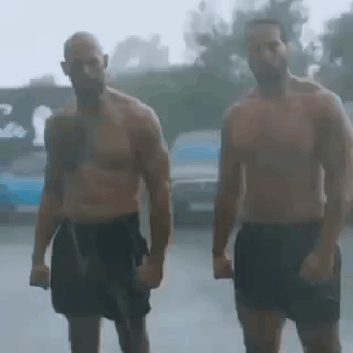 Two Shirtless Men Are Standing In The Rain Holding Hands . GIF