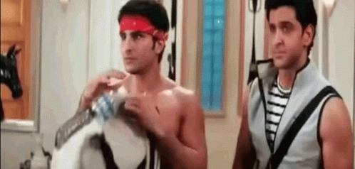 Two Shirtless Men Are Standing Next To Each Other In A Room . One Of The Men Is Wearing A Red Headband . GIF