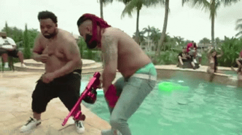 Two Shirtless Men Holding Pink Gun in Pool