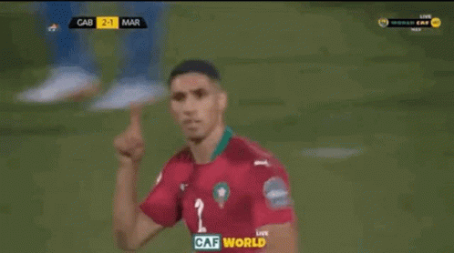 two soccer players are celebrating a goal in front of a large screen that says caf world on it