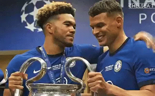 Two Soccer Players Are Holding A Trophy In A Locker Room . GIF