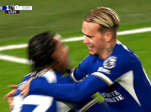Two Soccer Players Are Hugging Each Other On A Field With A Score Of 1:0 GIF