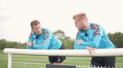 Two Soccer Players Are Leaning On A Fence Talking GIF
