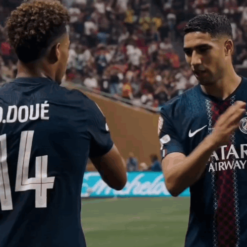 two soccer players are shaking hands and one has the number 14 on his jersey